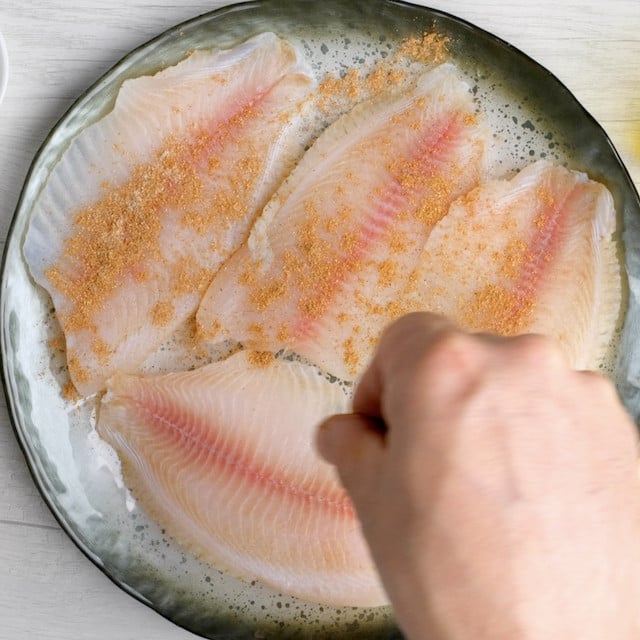 Seasoning being sprinkled on tilapia fillets to make pan seared tilapia.
