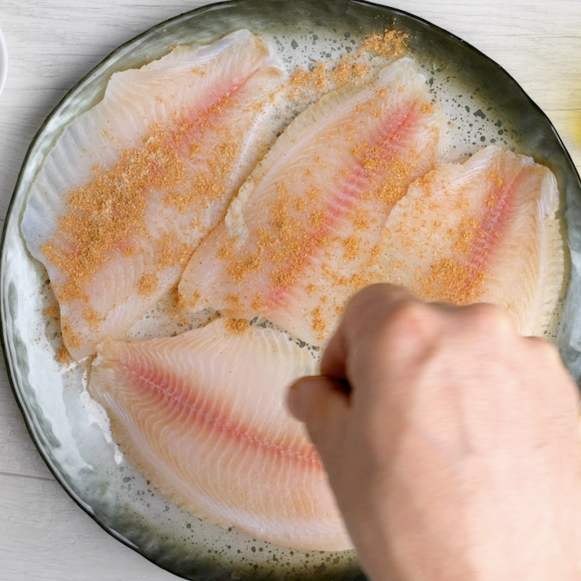 Seasoning being sprinkled on tilapia fillets to make pan seared tilapia.