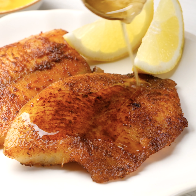 Lemon butter sauce being poured over pan seared tilapia.