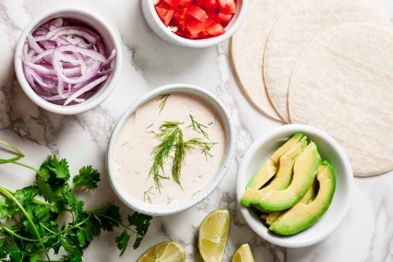 Overhead shot of ingredients and toppings to make crispy baja fish tacos at home.