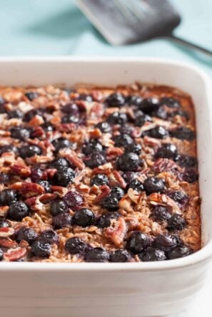 Gluten-free Baked Blueberry Oatmeal in a white dish, topped with blueberries and chopped pecans, makes a healthy breakfast.