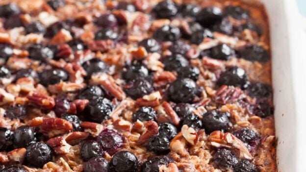 Gluten-free Baked Blueberry Oatmeal in a white dish, topped with blueberries and chopped pecans, makes a healthy breakfast.