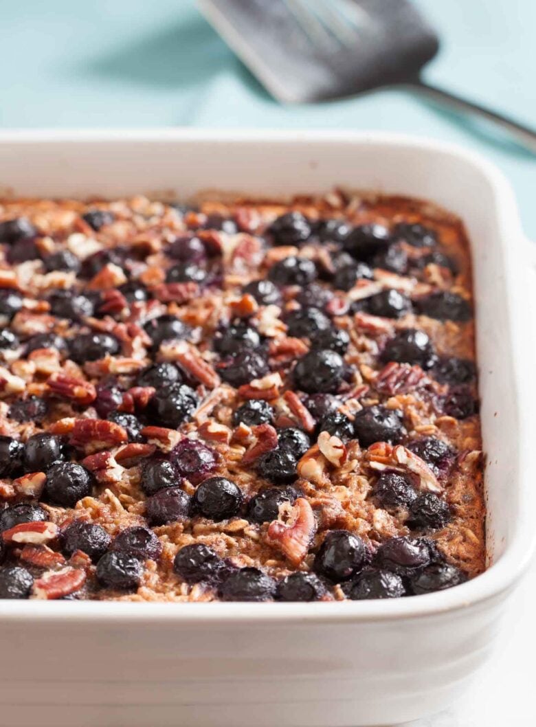 Gluten-free Baked Blueberry Oatmeal in a white dish, topped with blueberries and chopped pecans, makes a healthy breakfast. 