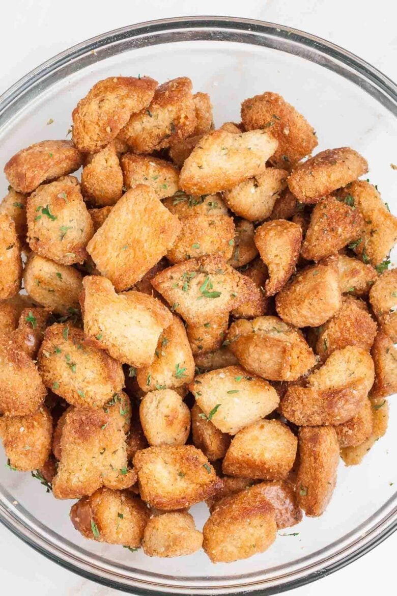 A glass bowl filled with golden brown, crispy garlic croutons garnished with chopped herbs.