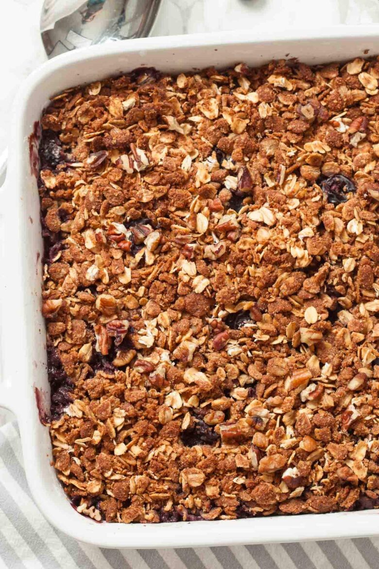 A Healthy Blueberry Crumble baked in a white rectangular dish, featuring a golden brown oat and nut topping.
