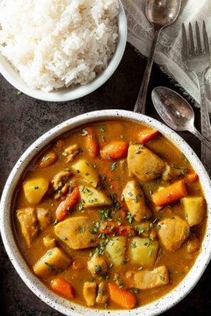 A bowl of hearty Japanese chicken curry with potatoes and carrots, next to a bowl of fluffy white rice.