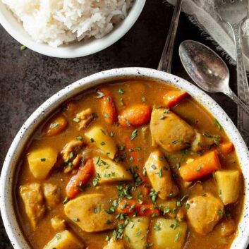 A bowl of hearty Japanese chicken curry with potatoes and carrots, next to a bowl of fluffy white rice.