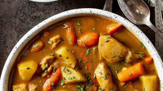 A bowl of hearty Japanese chicken curry with potatoes and carrots, next to a bowl of fluffy white rice.