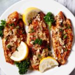 Three fillets of flaky rockfish topped with lemon garlic sauce, garnished with lemon wedges and fresh parsley.