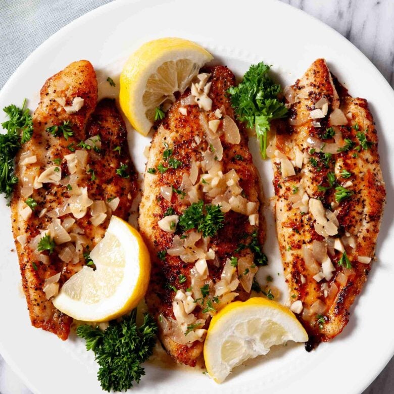Three fillets of flaky rockfish topped with lemon garlic sauce, garnished with lemon wedges and fresh parsley.
