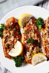 Three fillets of flaky rockfish topped with lemon garlic sauce, garnished with lemon wedges and fresh parsley.