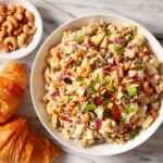 Overhead shot of chicken curry salad in a bowl with croissants and roasted cashews on the side.