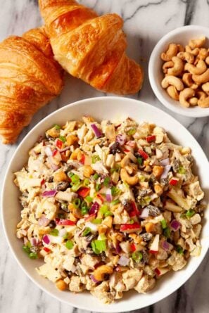 Overhead shot of chicken curry salad in a bowl with croissants and roasted cashews on the side.