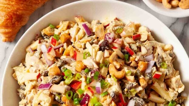 Overhead shot of chicken curry salad in a bowl with croissants and roasted cashews on the side.