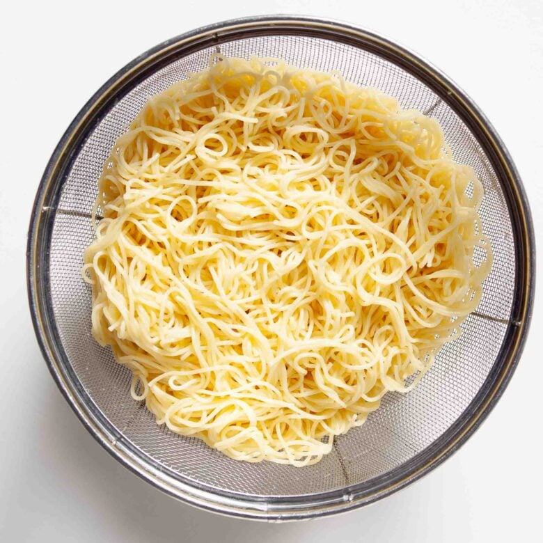 Cooked angel hair pasta in a metal sieve.