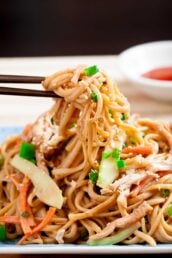 Closeup of chopsticks holding cold sesame noodles, with toasted sesame and thinly sliced green onions on top.