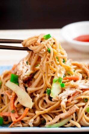 Closeup of chopsticks holding cold sesame noodles, with toasted sesame and thinly sliced green onions on top.
