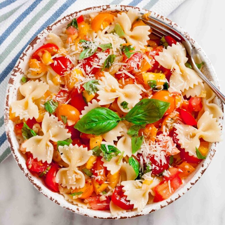 Overhead shot of a bowl with fresh tomato basil pasta with fresh basil leaves and visible tomato chunks.