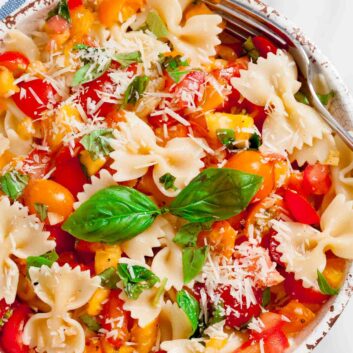 Overhead shot of a bowl with fresh tomato basil pasta with fresh basil leaves and visible tomato chunks.