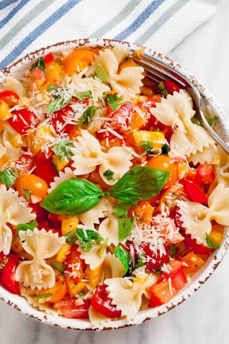 Overhead shot of a bowl with fresh tomato basil pasta with fresh basil leaves and visible tomato chunks.