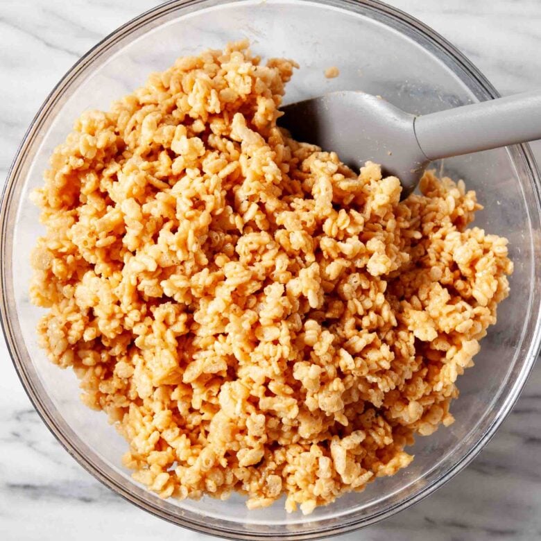 Crispy rice cereal added to peanut butter and honey mixture in a glass bowl to make healthy rice krispie treats.