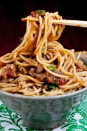 Chopsticks hold Mongolian beef noodles over a bowl.