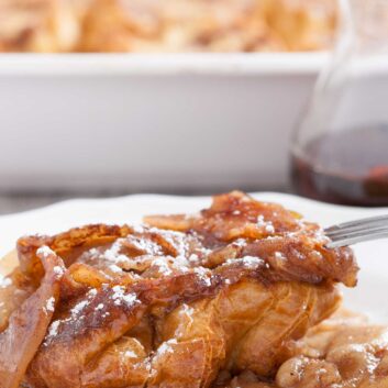 A slice of make-ahead apple french toast casserole on a white plate, with a fork.
