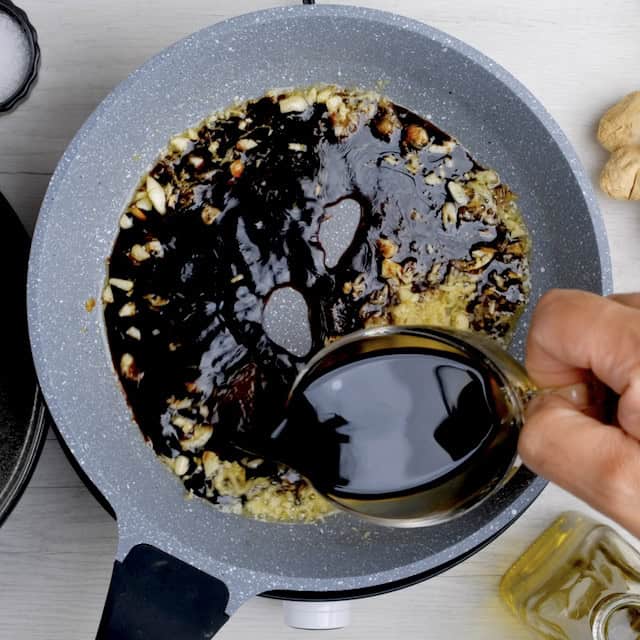 Soy sauce being poured into a pan with sautéed aromatics, to make Mongolian beef recipe at home.
