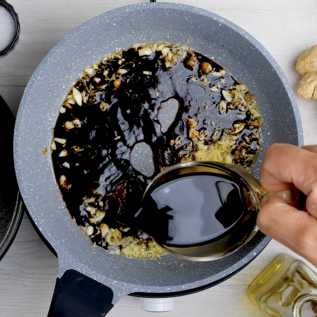Soy sauce being poured into a pan with sautéed aromatics, to make Mongolian beef recipe at home.