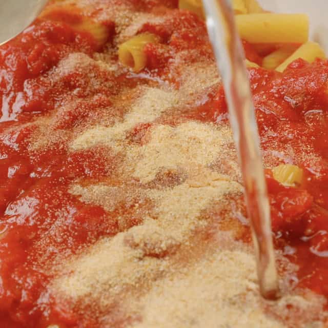 Broth being poured into baking dish with marinara, uncooked pasta, and seasonings.