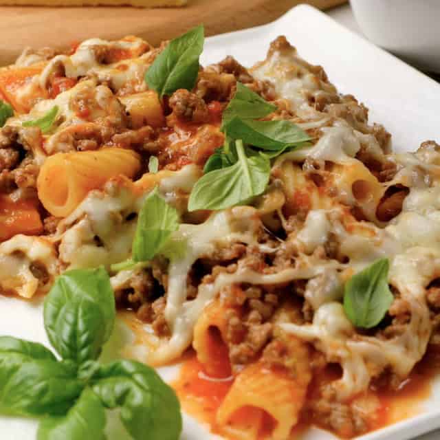 Freshly made baked rigatoni in a white plate with basil for garnish.