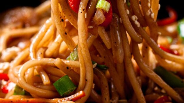 Closeup shot of lo mein noodles being held by chopsticks.