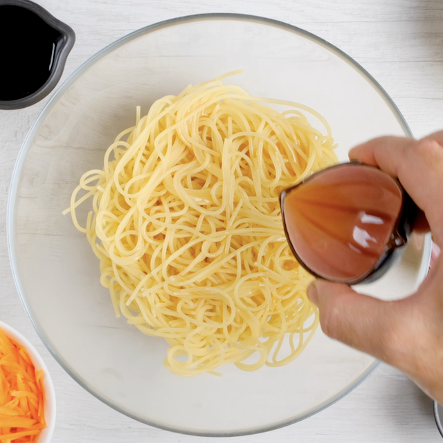 Sesame oil being added to cooked noodles.