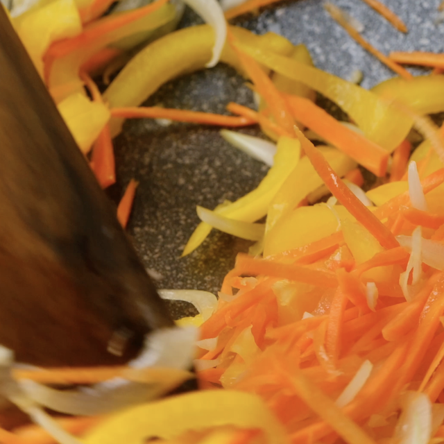 Sliced carrots and bell peppers being cooked in a pan.