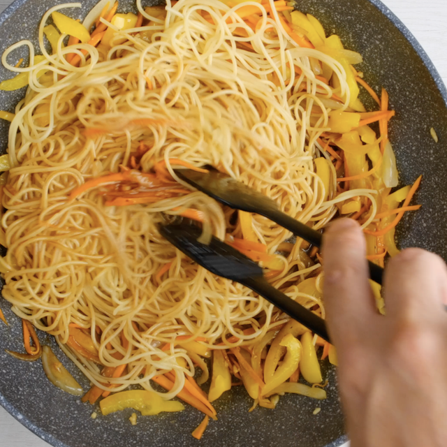 Lo mein noodles with sauce being tossed before serving.