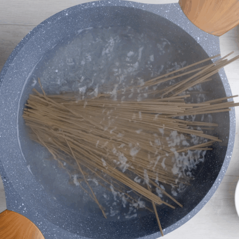 Soba noodles being boiled in a pot of hot water.