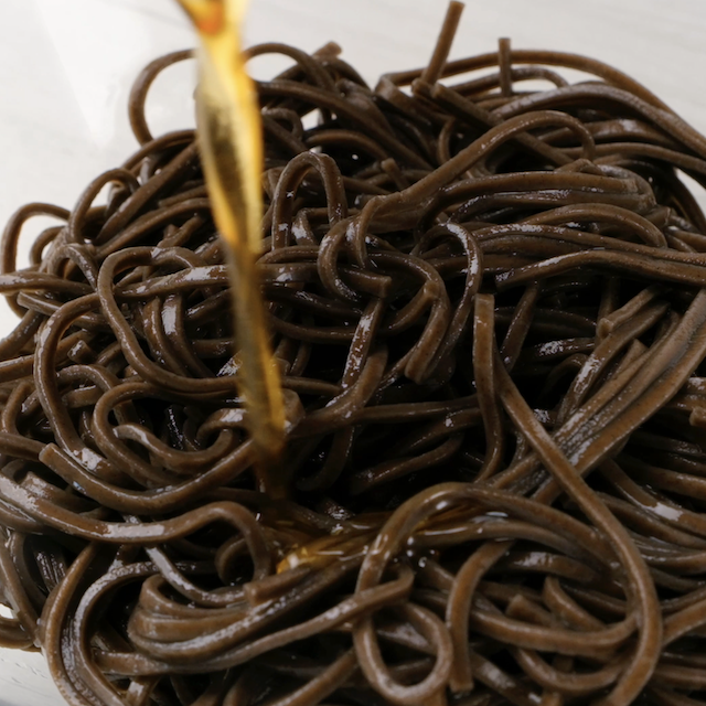 Cooked soba noodles being tossed with sesame oil.