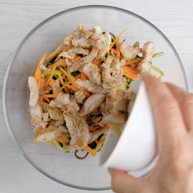Chicken, cucumber, and carrots being added to cooked soba noodles in a bowl.