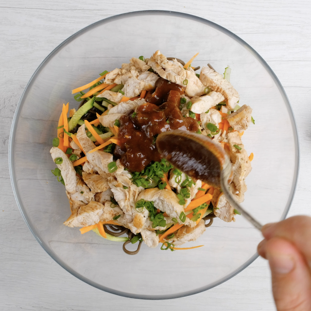 Peanut sauce being added to noodles, chicken, and veggies in a bowl to make peanut soba noodles with chicken.