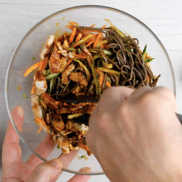 Peanut soba noodles with chicken being tossed with homemade peanut sauce before serving.