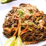 Peanut soba noodles with chicken, served with lime wedges on the side and a sesame seeds on top.