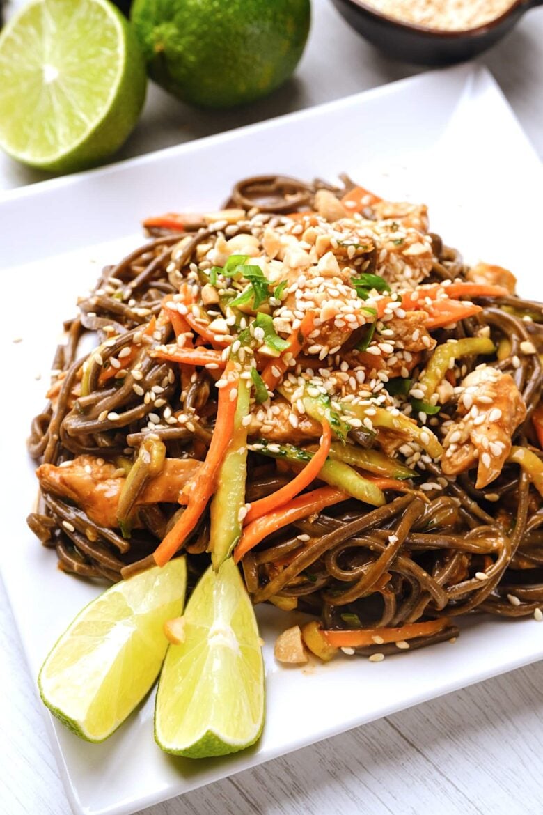Peanut soba noodles with chicken, served with lime wedges on the side and a sesame seeds on top.