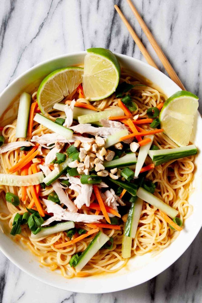 Overhead shot of peanut soba noodles with chicken, with lime wedges on the side.