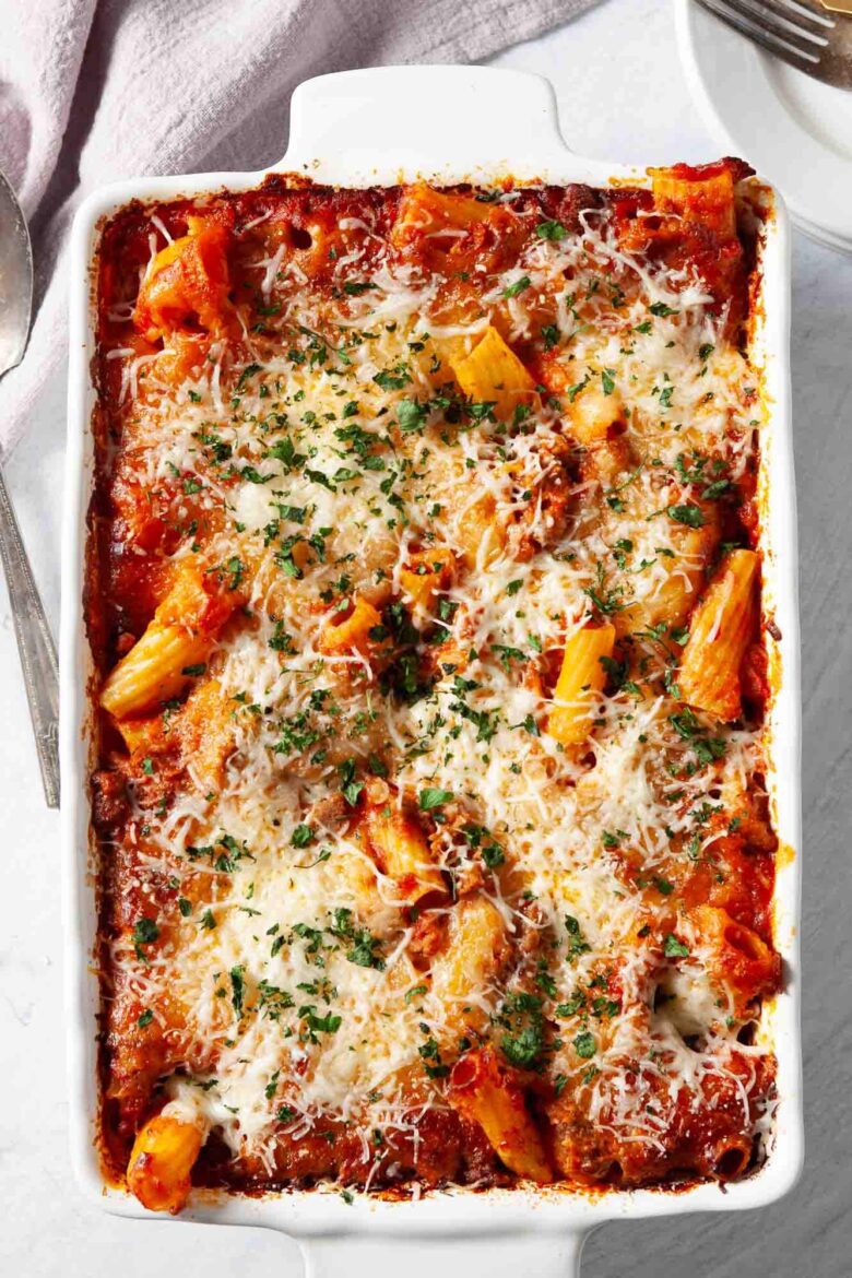 A baked rigatoni dish with savory sausage, marinara sauce, melted cheese, and herbs in a white rectangular baking dish.