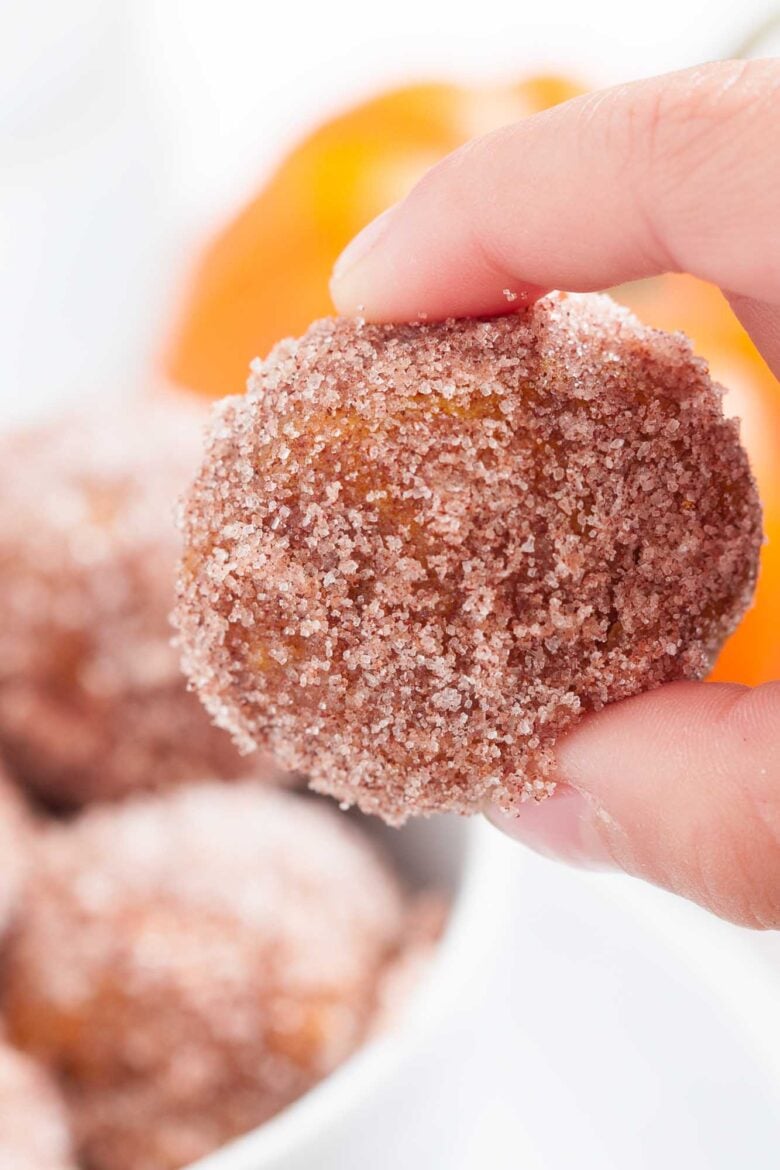 Closeup shot of a hand holding a pumpkin donut hole with cinnamon sugar topping.