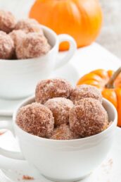 A bowl with freshly baked pumpkin donut holes, with more in the background.