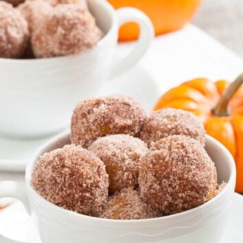 A bowl with freshly baked pumpkin donut holes, with more in the background.