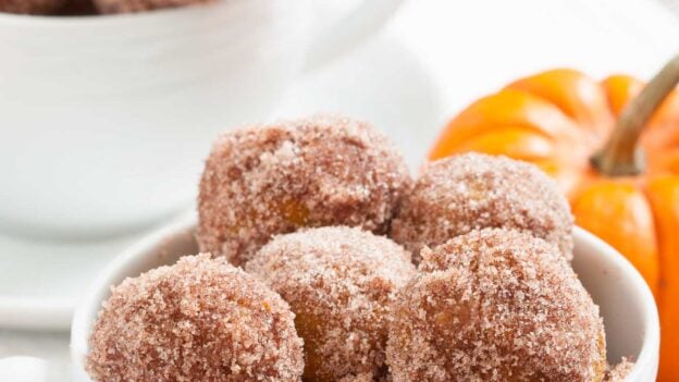 A bowl with freshly baked pumpkin donut holes, with more in the background.