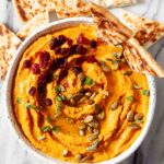 pumpkin hummus with garnish such as pepitas and dried cranberries in a bowl.