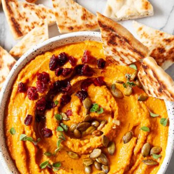 pumpkin hummus in a bowl, garnished with pepitas, dried cranberries, and pita chips.